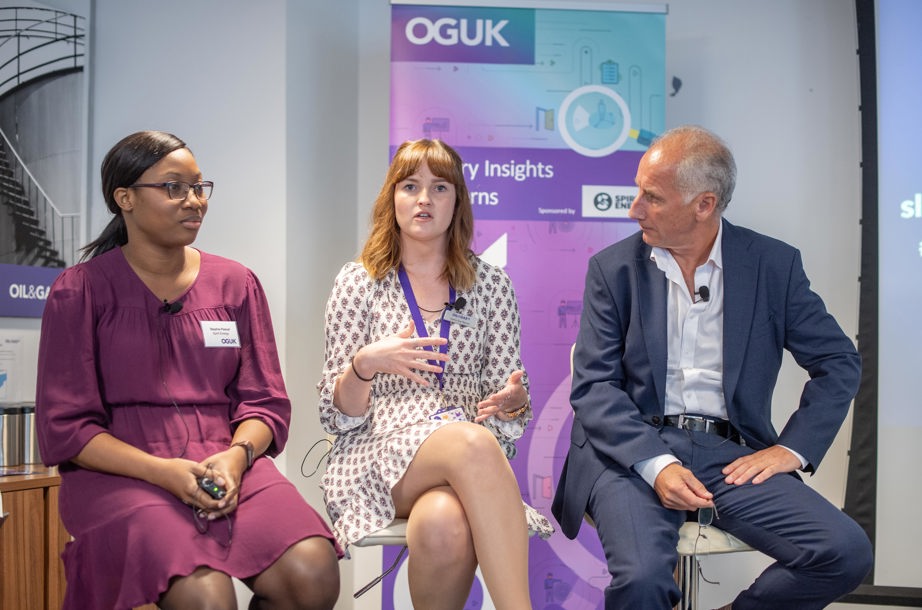 Three people sitting in front of a sign that says 'OGUK'