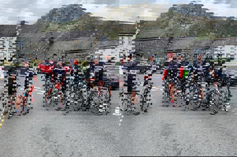 A group of cyclists posing for the camera. The background shows houses and a mountain..