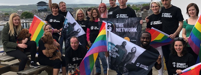 A group of Spirit Energy employees standing on a balcony, posing with pride flags and umbrellas