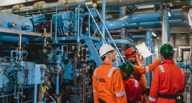 Workers in overalls and safety helmets in front of machinery