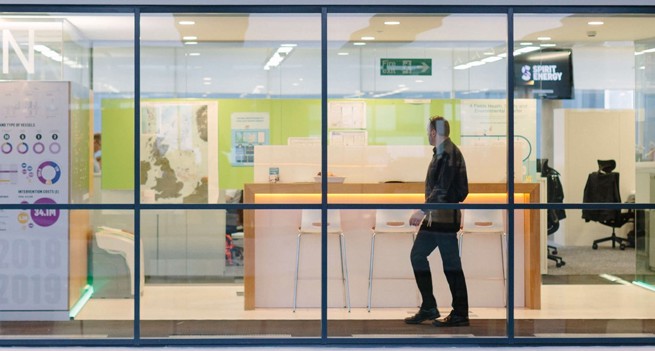 A wide shot of a Spirit Energy office as seen through a curtain wall. Inside, there are chairs, tables, and a person who's walking.